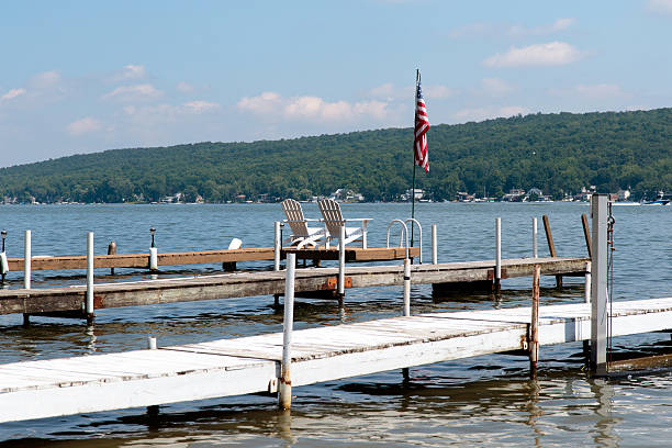 Docks on a lake Color DSLR image of docks on Conesus Lake with adirondack chairs and a flag finger lakes stock pictures, royalty-free photos & images