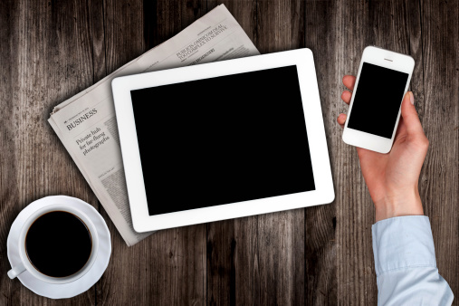 smartphone in hand and a newspaper with the tablet on the table