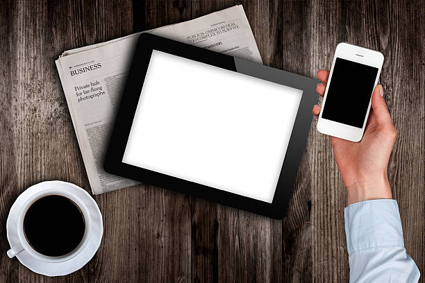 smartphone in hand and a newspaper with the tablet on the table