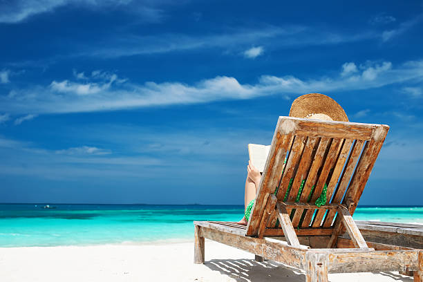 istock Young woman reading a book at beach 496617409