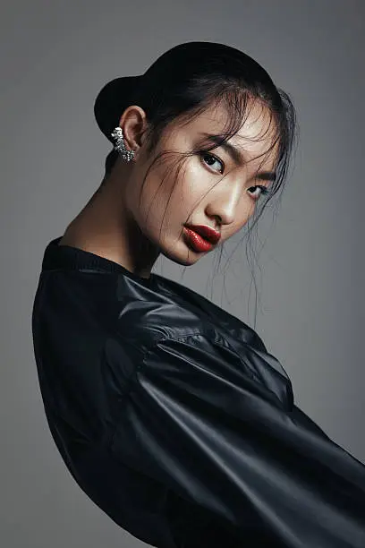 Portrait of fashionable asian woman wearing leather top and statement ear cuff. Professional make-up and hairstyle. High-end retouch.