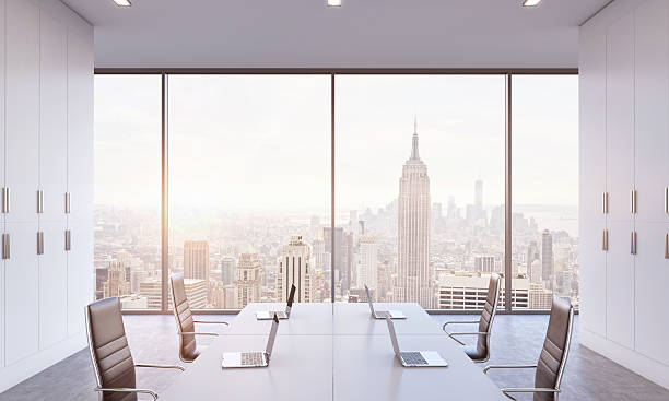 conference area in a bright modern open space office. Workplaces or conference area in a bright modern open space office. White tables equipped by modern laptops and black chairs. New York view. 3D rendering. A sunset. Toned image. late modern period stock pictures, royalty-free photos & images