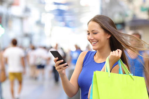 Shopper woman shopping with a smartphone in a commercial street