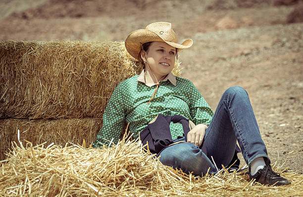 Cowgirl Cowgirl woman smiling happy sitting next to haystack wearing cowboy hat. Beautiful young Caucasian girl in countryside woman lying on hay bale stock pictures, royalty-free photos & images
