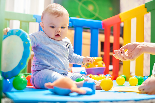 A young baby boy sits playing in his brightly coloured playpen. He discovering how to move and play with his toys. The bright colours, sounds and different textures of the toys are building his sensory perceptions.