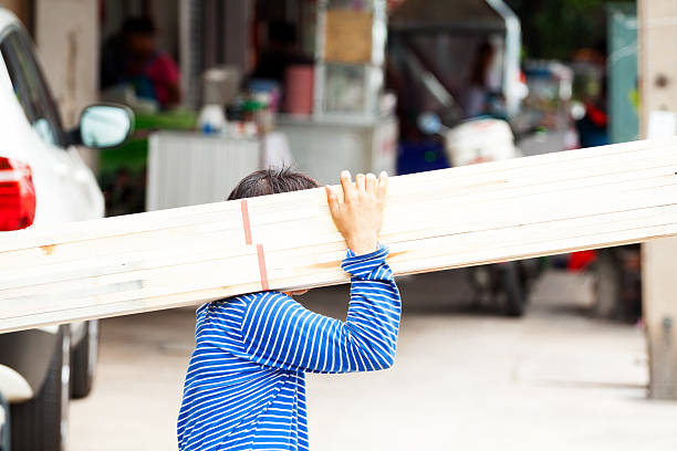 Bangkok, Thailand - April, 29th 2014: A Thai man is carrying wooden planks on shoulder crossing sidewalk. Man is bringing wood from store to truck. Scene is in street Chokchai 4 in Ladprao.