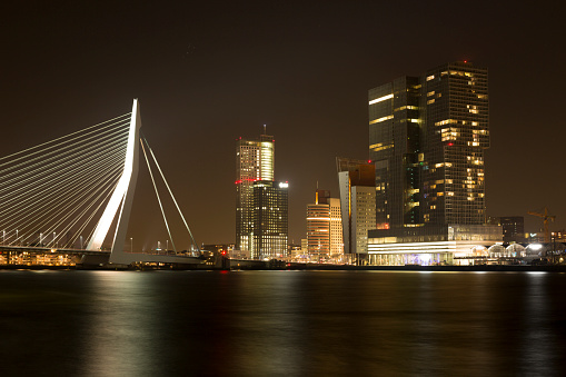 Rotterdam, The Netherlands – October 10, 2015:  Erasmus Bridge with the Rotterdam skyline in the background at night, reflecting in the river Meuze.