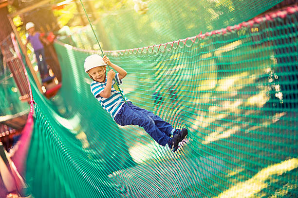 Little boy zipping in adventure park Little boy zipping on zip line in outdoors amusement park. The smiling boy aged 6 is wearing a helmet. canopy tour photos stock pictures, royalty-free photos & images
