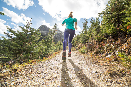 Low angle of woman running uphill towards sunlight. Rear view, focus on the sole of shoe.
