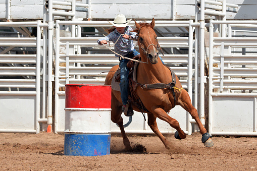 Young girl in western attire riding a horse around a barrel in a race during a rodeo.