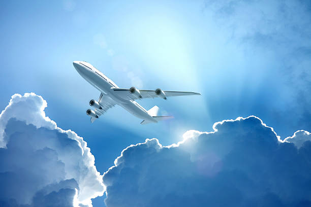 istock White jet airplane flying over the clouds with sun beams 496662326