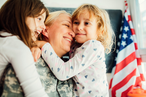 Military mom hugging with her two children, little girls. They are hugging each other, smiling with tears of joy. Having some happy time together. Mother just return from some of army missions. Shot with Canon EOS 5Ds 50mp