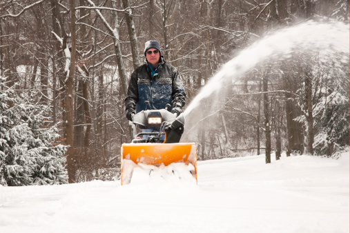 Man pushing snowblower on residential driveway