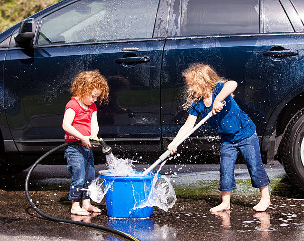 Two Young Girls Washing Car Two young girls (sisters) having fun washing the car together. The younger sister is spraying water into the bucket, while the older sister dips her scrub brush into the bucket. cropped pants photos stock pictures, royalty-free photos & images