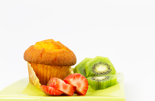 Delicious corn muffin with slices of kiwi and strawberry.  Healthy, tasty fruit and baked food on green plate.