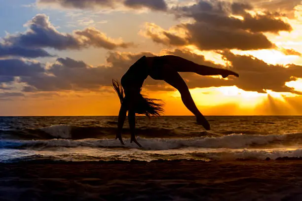 Silhouette of woman doing a back flip on a beach