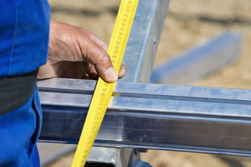 Close up of construction worker using measure tape on steel construction frame