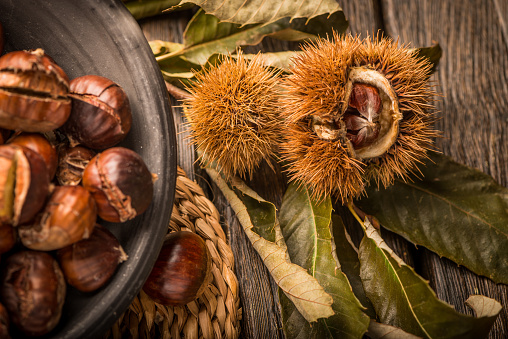 Roasted chestnuts on a rustic wooden table with autumn leaves in the background.