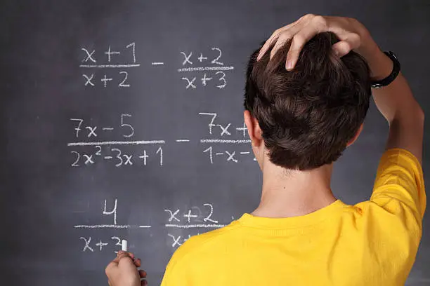 Young student scratching his head in front of blackboard