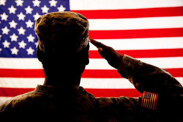 Silhouette of soldier saluting the American flag A military veteran salutes her American flag.  The patriotic veteran wears a military uniform, and she faces the flag with honor and respect.  The silhouette of the solider is shown against a red, white and blue flag background.  There is a flag patch on the sleeve of the woman's military uniform. in pride we trust stock pictures, royalty-free photos & images