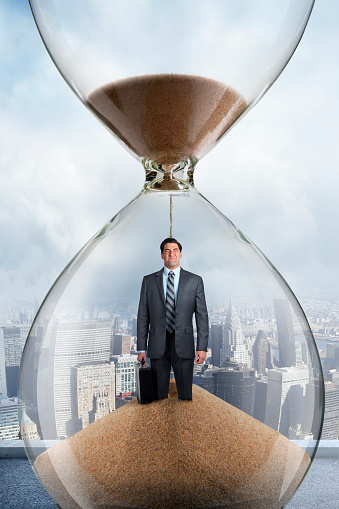 Sand pouring through an hourglass lands on the head of a businessman who is standing inside the hourglass.