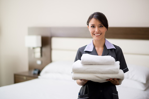 Maid working at a hotel holding towels and looking at the camera smiling - housekeeping concepts