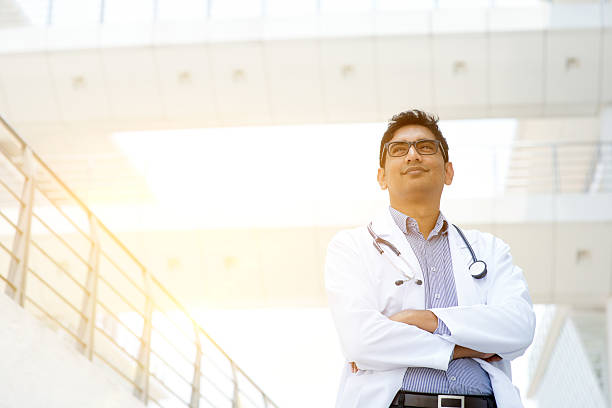 Asian medical doctor portrait Portrait of confident Asian Indian medical doctor standing outside hospital building, beautiful golden sunlight at background. india hospital stock pictures, royalty-free photos & images