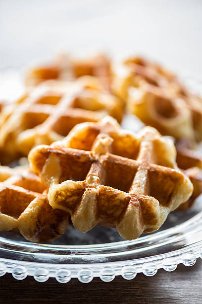 Glass Plate of Mini Belgium Liege Waffles on Wood Table Closeup view of freshly made bite sized, small Belgium Liege waffles on a clear, decorative glass plate set on a wooden table. liege belgium stock pictures, royalty-free photos & images