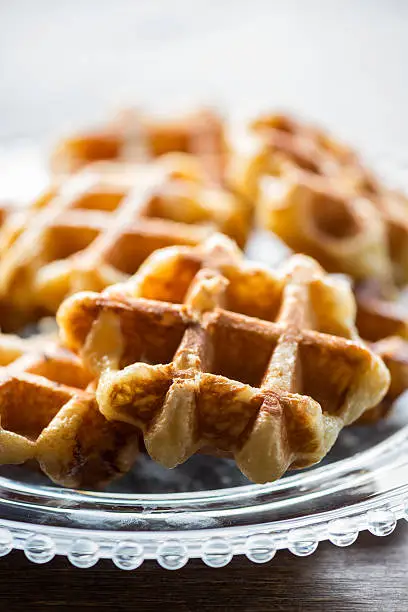 Closeup view of freshly made bite sized, small Belgium Liege waffles on a clear, decorative glass plate set on a wooden table.