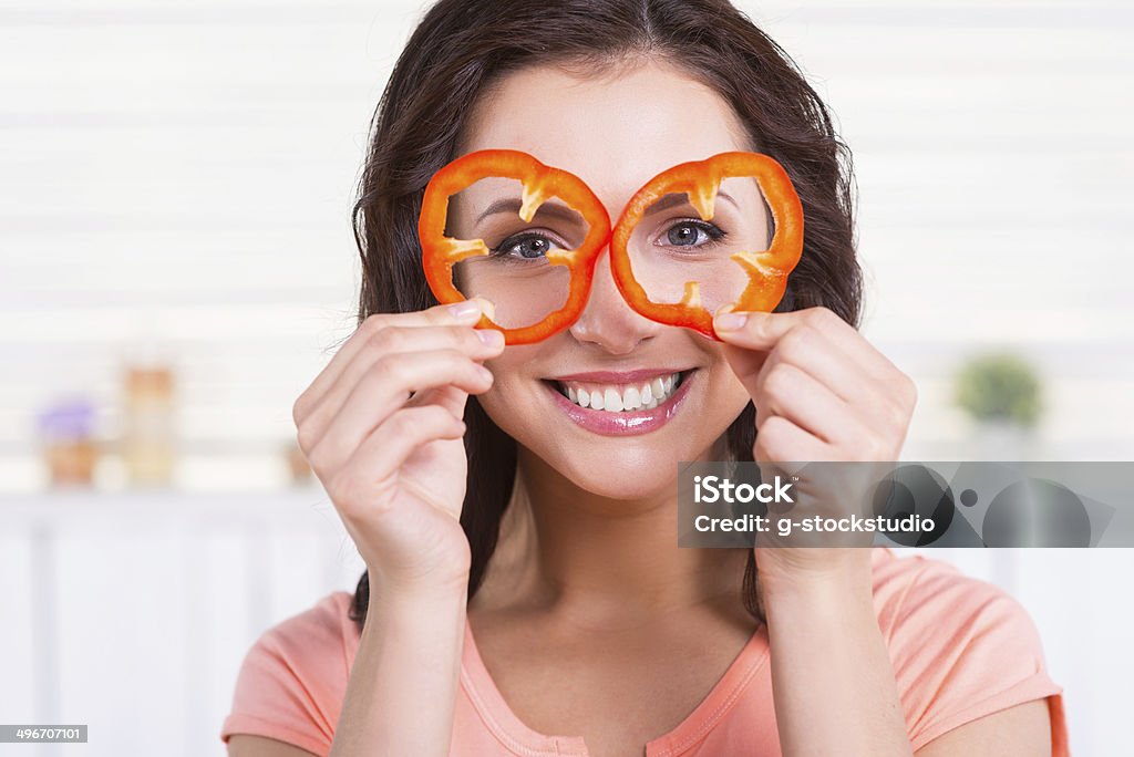 Kitchen fun. Portrait of playful young woman looking through the pieces of red pepper and smiling while standing in the kitchen Adult Stock Photo