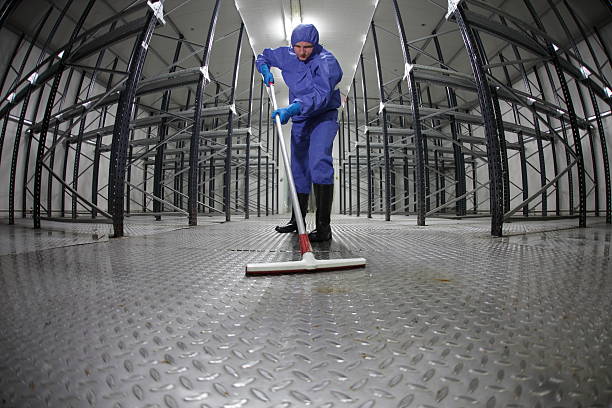 worker in protective uniform cleaning floor in empty storehouse stock photo