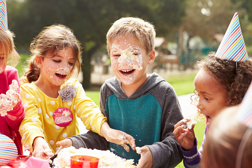 Group Of Children Having Outdoor Birthday Party With Bithday Cake On Faces
