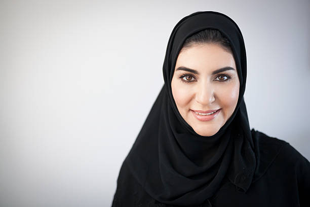 Smiling Middle Eastern Woman Portrait Young middle eastern woman dressed in black religious veil pleasantly smiling and looking at the camera. Dark brown eyes and hair, glowing skin, warm look. Light grey background darkened around the corners. Image contains plenty of copy space on the left. Made in Dubai, United Arab Emirates. arab woman stock pictures, royalty-free photos & images