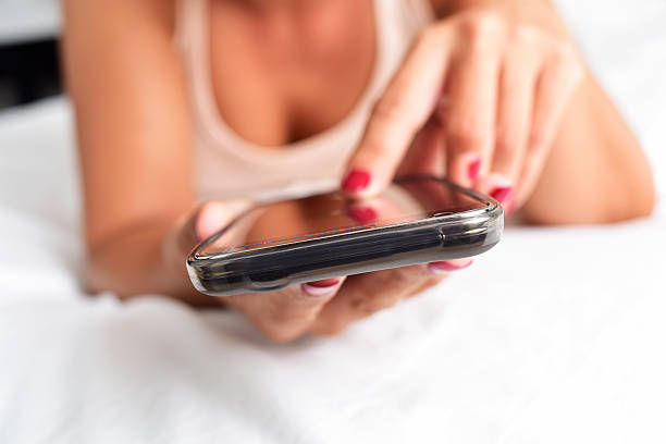 young woman using a smartphone in bed stock photo
