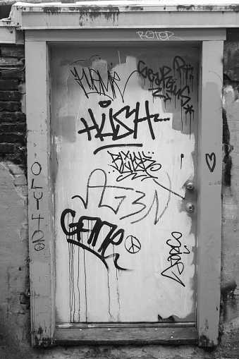This black and white image shows graffiti and tags painted on a business door in an alley in downtown Seattle, Washington.