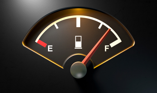 A closeup of a backlit illuminated gas gage with the needle indicating a near full tank on an isolated dark background