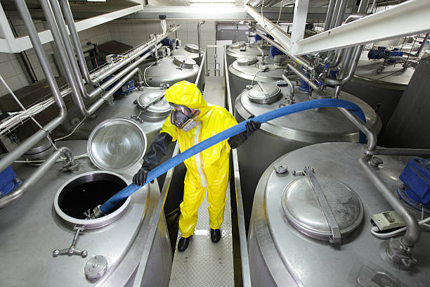 worker in coveralls filling large silver tank in factory stock photo