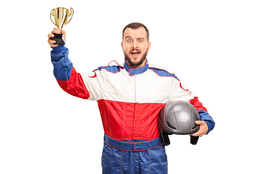 Studio shot of a joyful car racer holding a golden trophy and looking at the camera isolated on white background