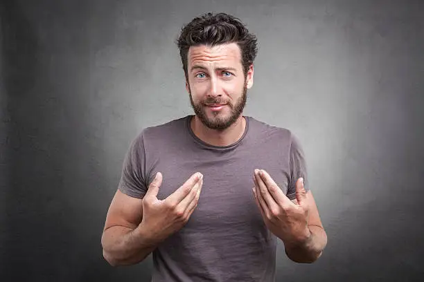 Frontal portrait of surprised adult man getting unexpected attention from people, asking you talking to, mean me? pointing finger at himself isolated on grey background. Facial expression body language