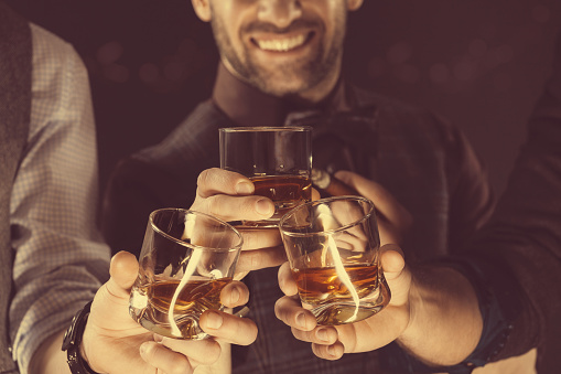 Three men drinking whiskey. Close up of glasses and hands. Dark tone. 