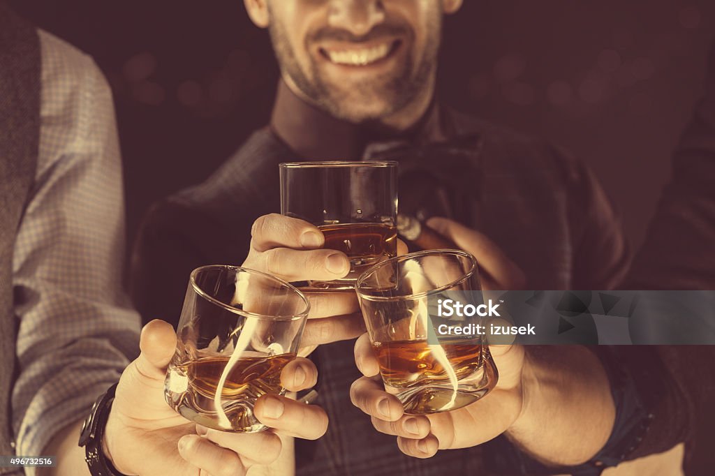 Men drinking whiskey, close up of glasses and hands Three men drinking whiskey. Close up of glasses and hands. Dark tone.  Whiskey Stock Photo
