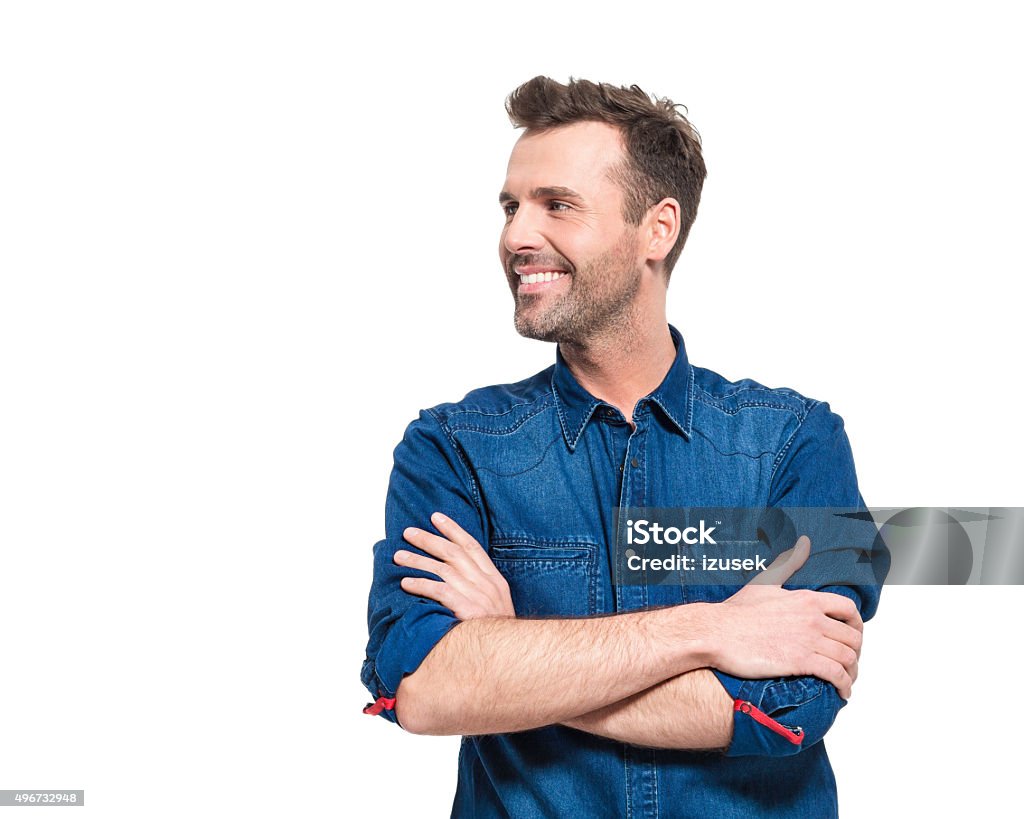 Portrait of happy man wearing jeans shirt Portrait of happy adult man wearing jeans shirt, standing against the white background with arms crossed, looking away.  Men Stock Photo