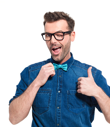 Portrait of excited adult man wearing jeans shirt, bow tie and nerd glasses, winking with mouth open. Studio shot, white background.