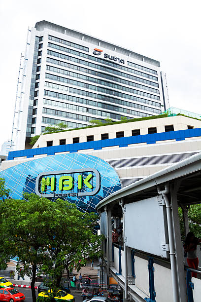 Bangkok, Thailand - July 16, 2013: Daytime shot of MBK mall in Bangkok. Some people are walking on pedestrian bridge. Down on street are  taxis and some people on sidewalk.