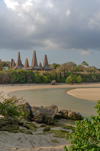 Ratenggaro traditional village in Kodi region in Sumba island, Indonesia. Vertical afternoon shot, from the beach, on a cloudy day, low tide.