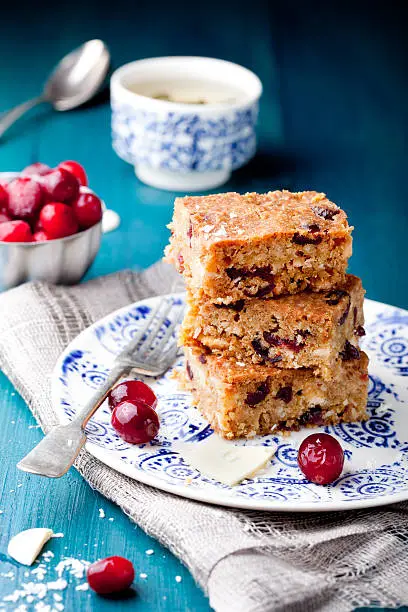 White chocolate cake, blondie, brownie with cranberry and coconut on a white and blue wooden background