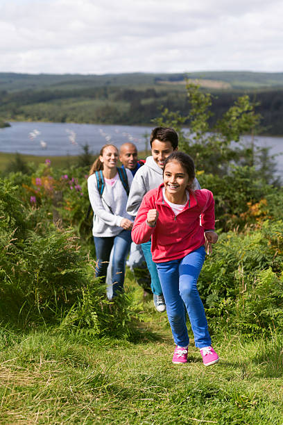 A family walk through the countryside together, the two children run ahead playfully chasing each other.