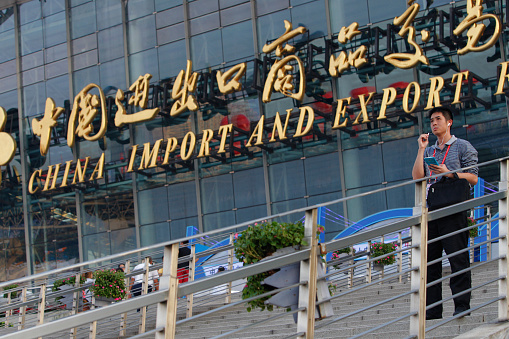 Guangzhou, Сhina - October 17, 2015: A man talks on his phone in front of China Import And Export Fair also known as Canton Fair witch started two days ago in Guangzhou, Guangdong province, October 17, 2015. The Canton Fair is a trade fair held in the spring and autumn seasons each year, and it's the largest trade fair in China.