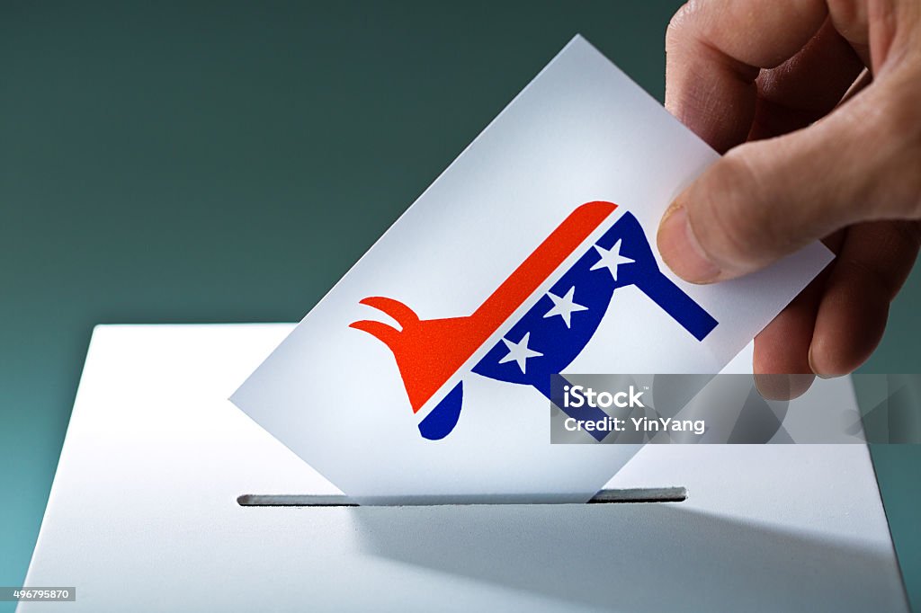 U.S. Election Voter Voting Democratic Party Ballot with Donkey Symbol Voter's hand holding election ballot for the U.S. Democratic Party with the donkey symbol, inserting the vote into the ballot box. Concept image of American democracy and the U.S. election process. Voters making their selection and putting in the voting ballot for the liberal Democratic Party. Photographed in  horizontal format. Democratic Party - USA Stock Photo