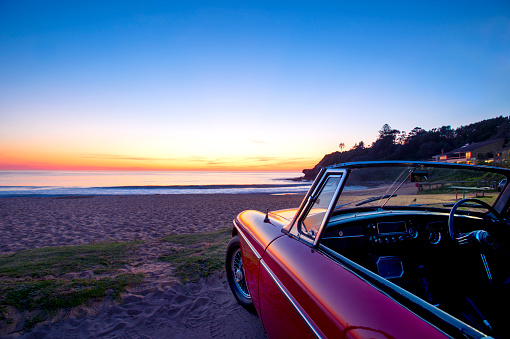 Convertible at the beach at sunset or sunrise. Car is parked on the sand looking at the view over the ocean. No people. Copy space.